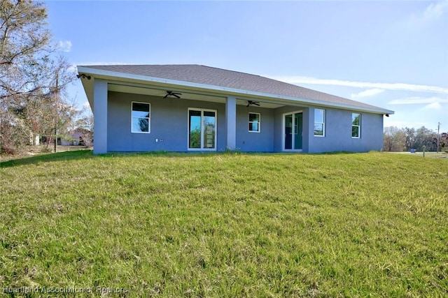 back of property featuring stucco siding, ceiling fan, and a yard