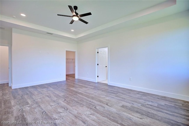 spare room with ceiling fan, recessed lighting, wood finished floors, baseboards, and a tray ceiling