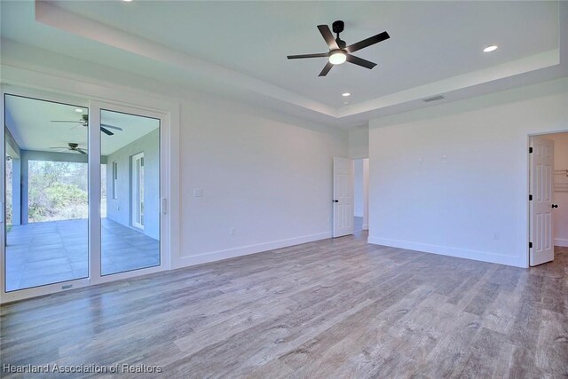 spare room featuring baseboards, a tray ceiling, wood finished floors, and recessed lighting