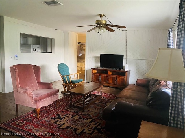 living area with visible vents, ceiling fan, wood finished floors, and wood walls