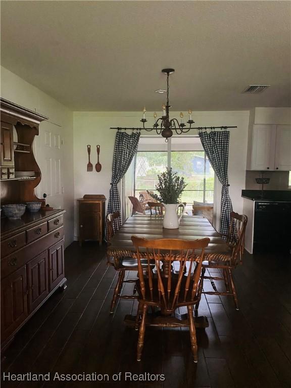 dining space featuring dark wood-style flooring, visible vents, and a notable chandelier