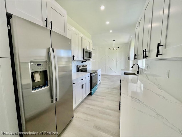 kitchen with light stone counters, stainless steel appliances, sink, pendant lighting, and white cabinetry