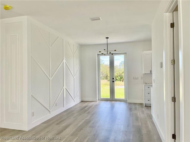 interior space with a notable chandelier, light wood-type flooring, and french doors