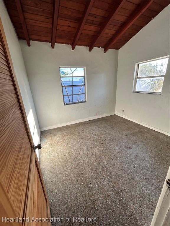 empty room with lofted ceiling with beams, wooden ceiling, carpet floors, and a wealth of natural light