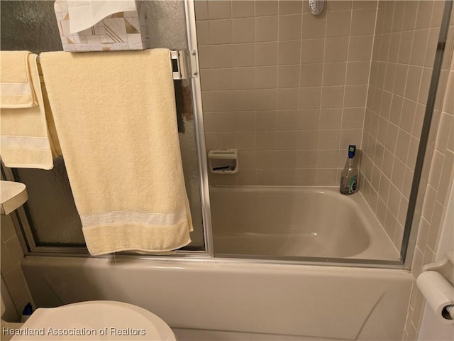bathroom with toilet and bath / shower combo with glass door