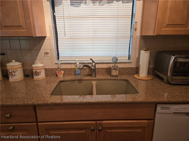 kitchen with stone countertops, white dishwasher, a sink, and decorative backsplash