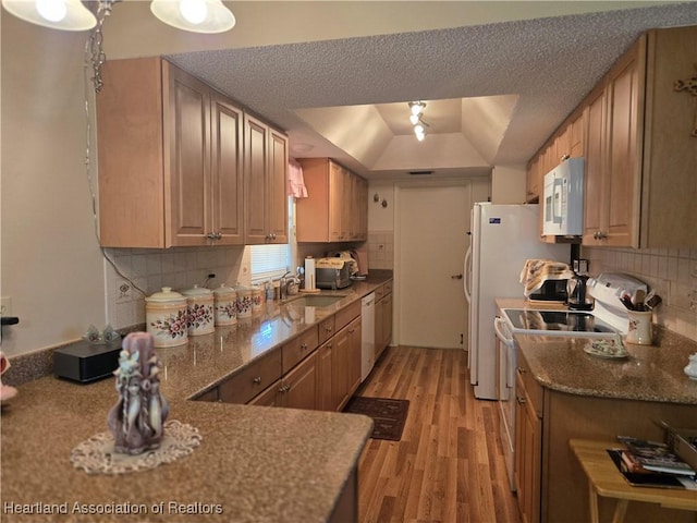 kitchen featuring a sink, light wood-type flooring, white appliances, decorative backsplash, and stone countertops