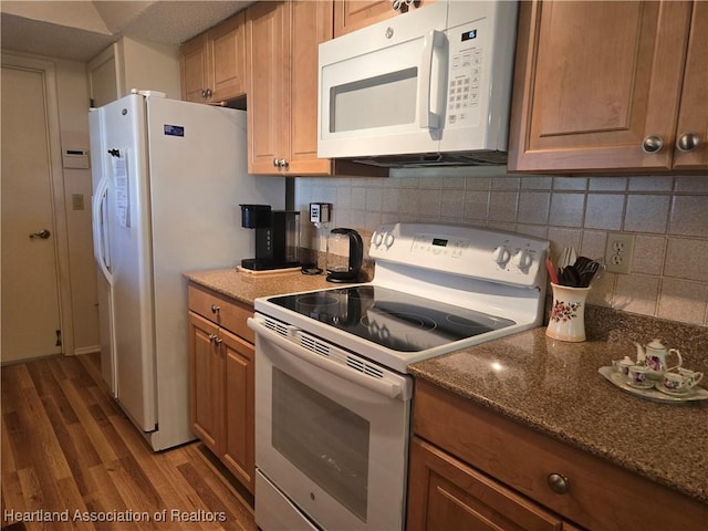 kitchen featuring dark stone countertops, white appliances, brown cabinetry, decorative backsplash, and wood finished floors