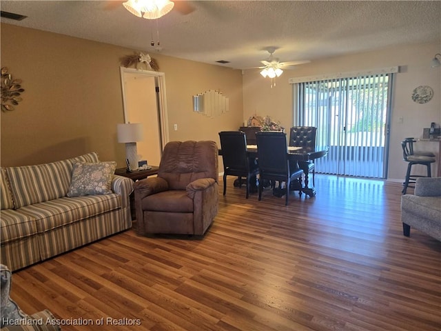 living room with a ceiling fan, wood finished floors, and a textured ceiling