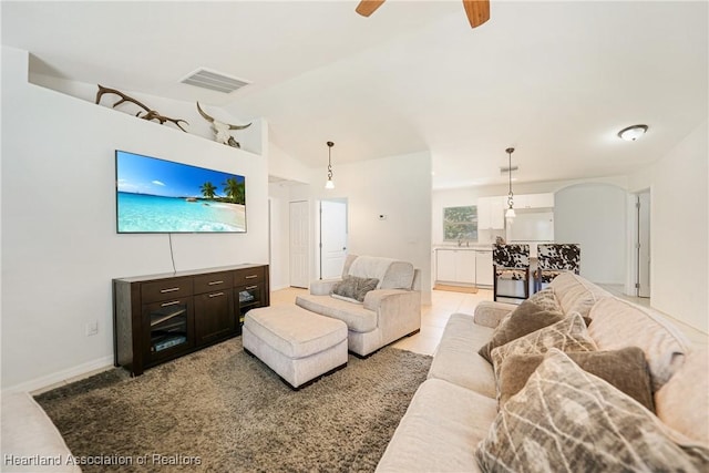 living area featuring light tile patterned floors, lofted ceiling, visible vents, ceiling fan, and baseboards