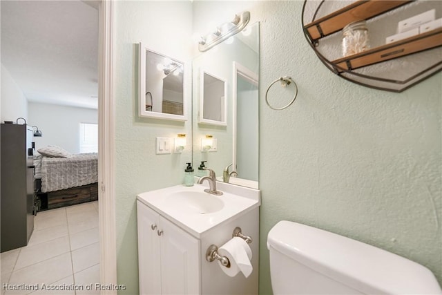 ensuite bathroom with connected bathroom, a textured wall, toilet, tile patterned flooring, and vanity