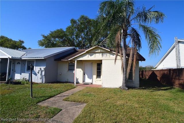 view of front of house featuring stucco siding, fence, metal roof, and a front yard