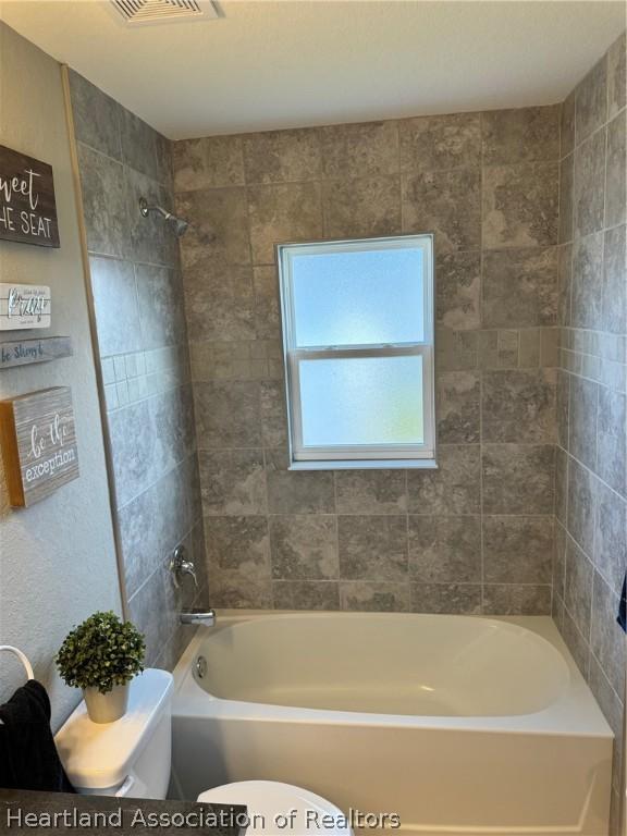 bathroom featuring tiled shower / bath combo and toilet