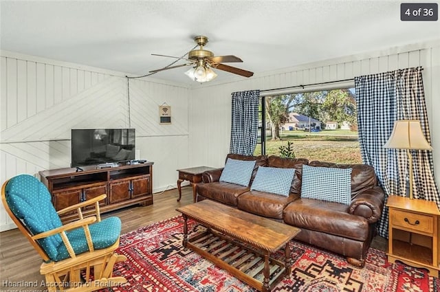 living room with hardwood / wood-style flooring, ceiling fan, and wooden walls