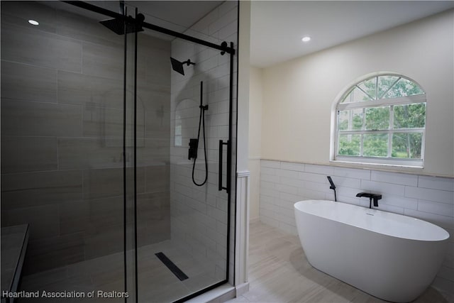 full bath with a wainscoted wall, recessed lighting, tile walls, a shower stall, and a soaking tub