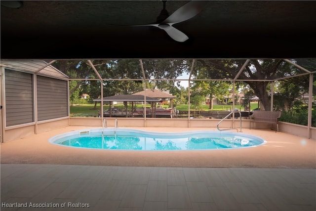 pool with glass enclosure, a patio, and a ceiling fan