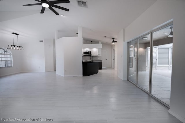 unfurnished living room featuring ceiling fan with notable chandelier, sink, and vaulted ceiling