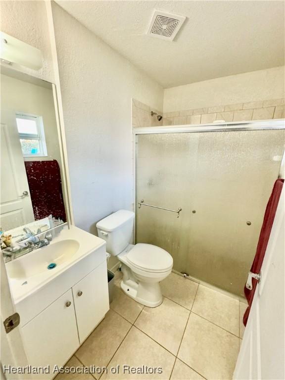 bathroom with toilet, vanity, tile patterned floors, and an enclosed shower