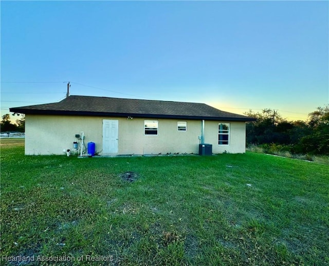 back of property featuring central air condition unit and a lawn