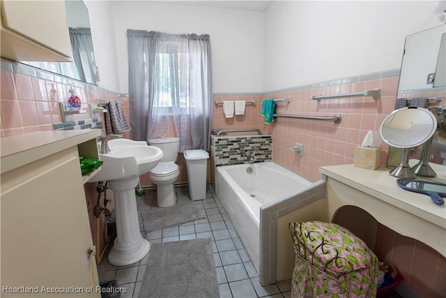 bathroom featuring tile patterned floors, toilet, sink, tile walls, and a bath