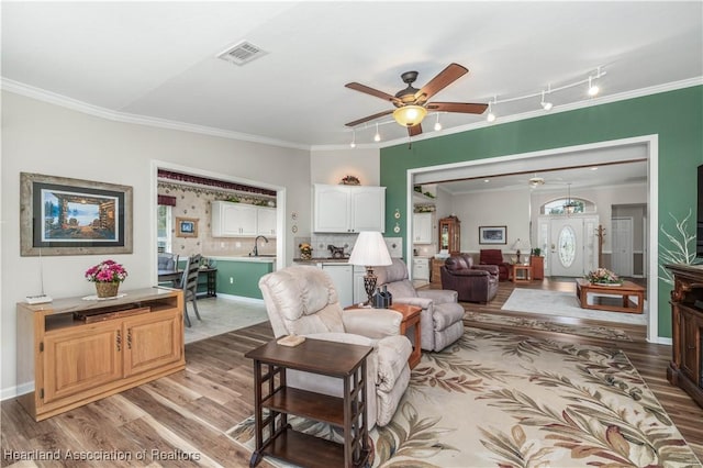 living room featuring rail lighting, ceiling fan, light wood-type flooring, and ornamental molding