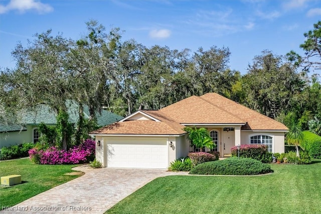 ranch-style home with a front yard, decorative driveway, an attached garage, and stucco siding