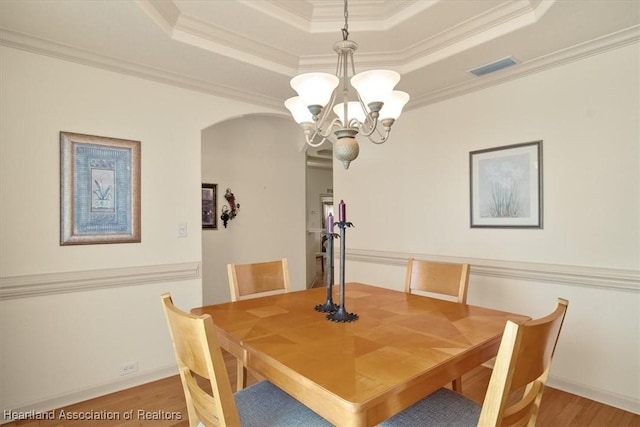 dining space featuring arched walkways, a raised ceiling, visible vents, ornamental molding, and wood finished floors