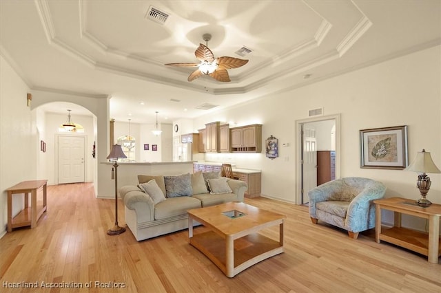 living room with a tray ceiling, visible vents, and arched walkways