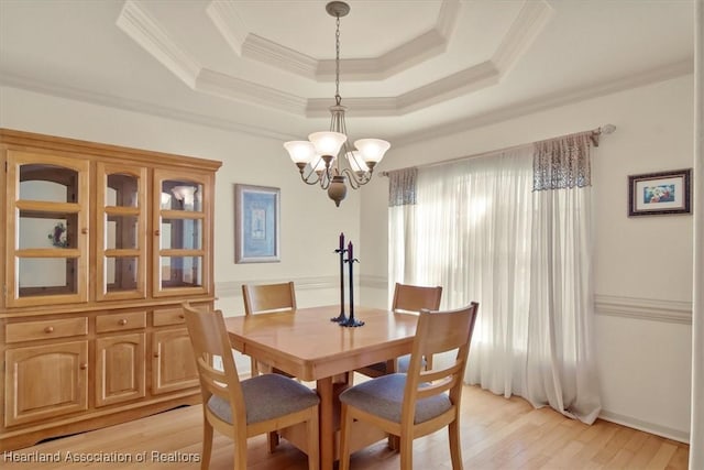 dining space with a tray ceiling, light wood-type flooring, an inviting chandelier, and crown molding