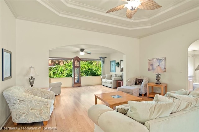 living room with ornamental molding, arched walkways, a raised ceiling, and wood finished floors