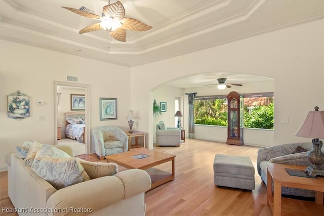 living area featuring arched walkways, light wood finished floors, a raised ceiling, visible vents, and ornamental molding