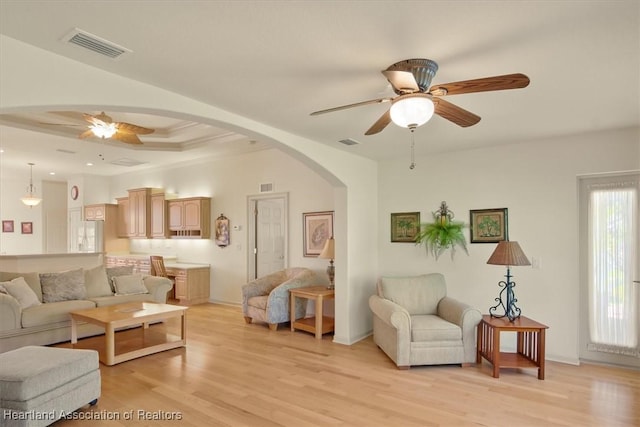 living room with arched walkways, visible vents, ceiling fan, and light wood finished floors