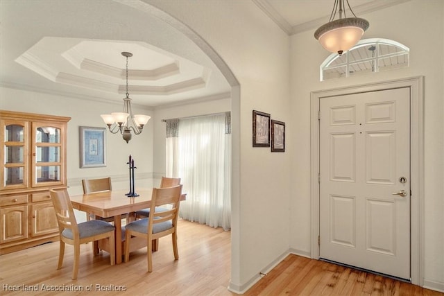 dining room featuring arched walkways, light wood-style flooring, ornamental molding, a tray ceiling, and an inviting chandelier