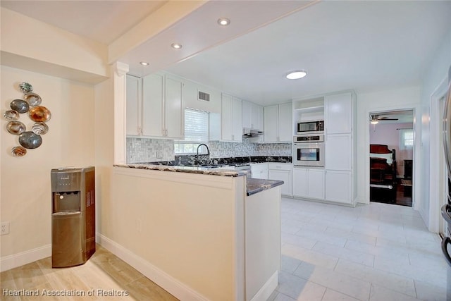 kitchen featuring kitchen peninsula, stainless steel appliances, white cabinetry, and dark stone counters