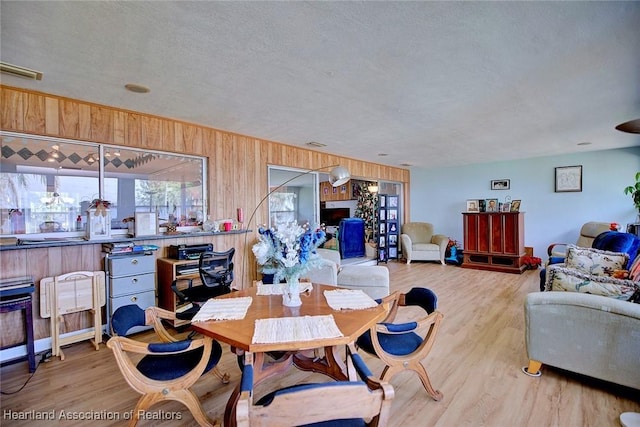 dining area featuring wooden walls, light hardwood / wood-style floors, and a textured ceiling