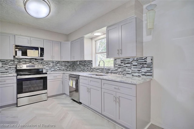 kitchen with backsplash, light parquet floors, sink, light stone countertops, and appliances with stainless steel finishes