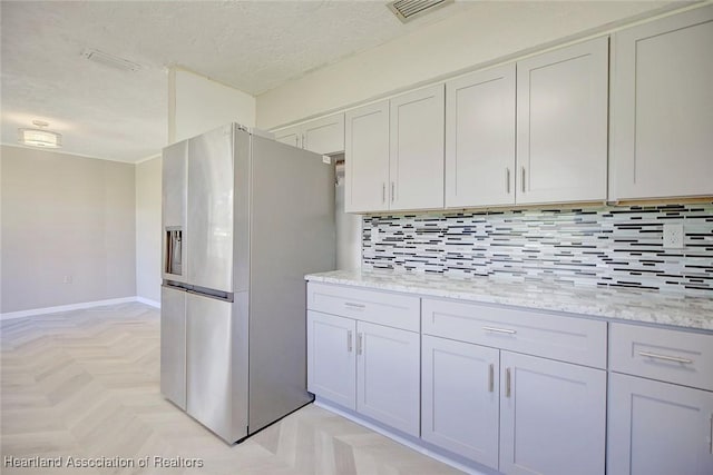 kitchen with white cabinetry, light stone countertops, stainless steel refrigerator with ice dispenser, decorative backsplash, and light parquet flooring