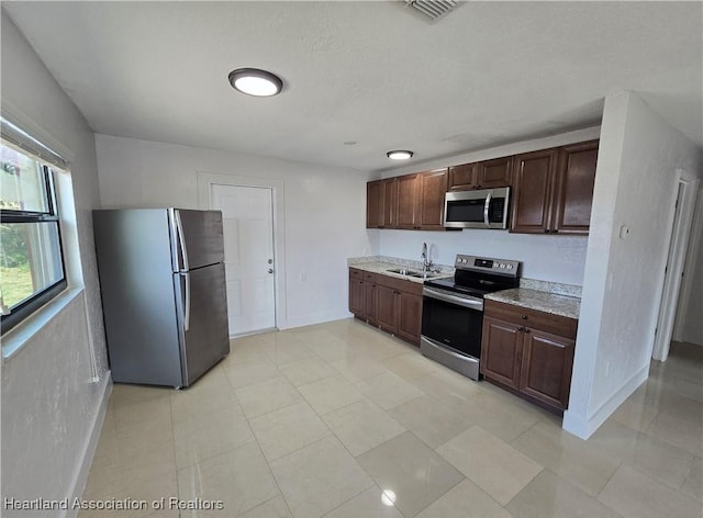 kitchen with light stone countertops, dark brown cabinets, stainless steel appliances, and sink