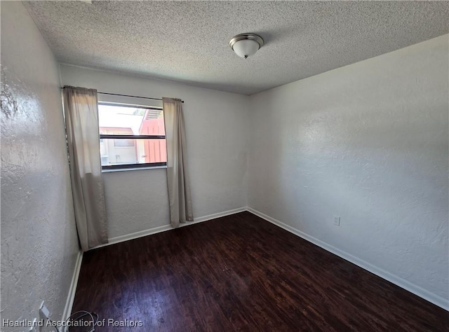 spare room featuring dark wood-type flooring and a textured ceiling