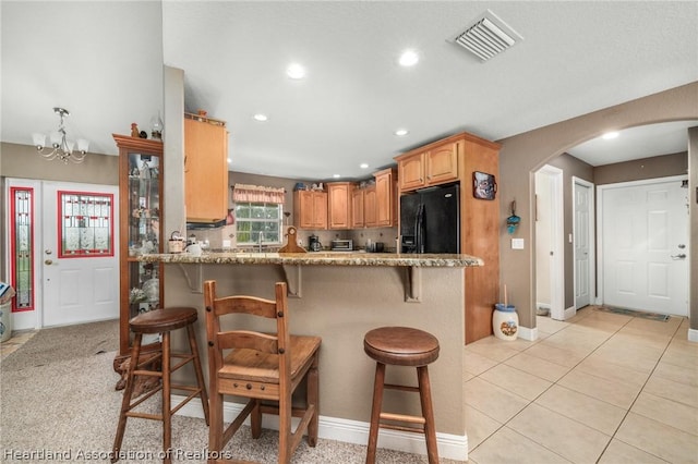 kitchen with kitchen peninsula, light stone countertops, black fridge, a notable chandelier, and a breakfast bar area