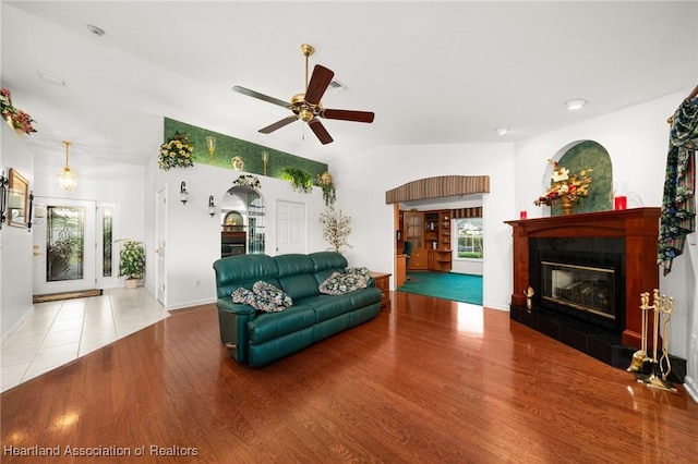 living room with lofted ceiling, baseboards, a tile fireplace, wood finished floors, and a ceiling fan