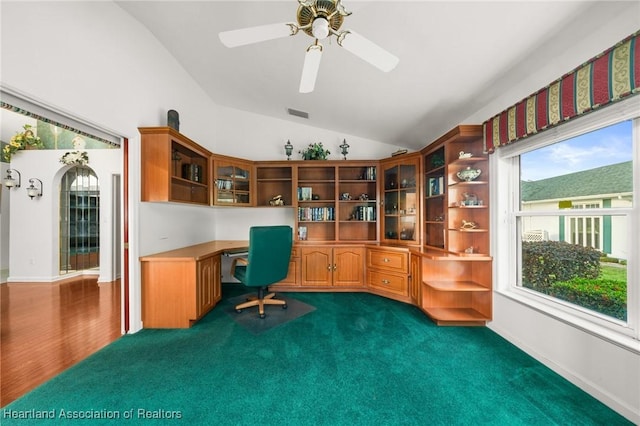 office area with built in desk, a ceiling fan, visible vents, dark carpet, and lofted ceiling