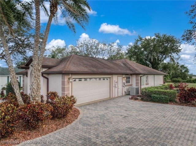 single story home with stucco siding, decorative driveway, central air condition unit, and an attached garage