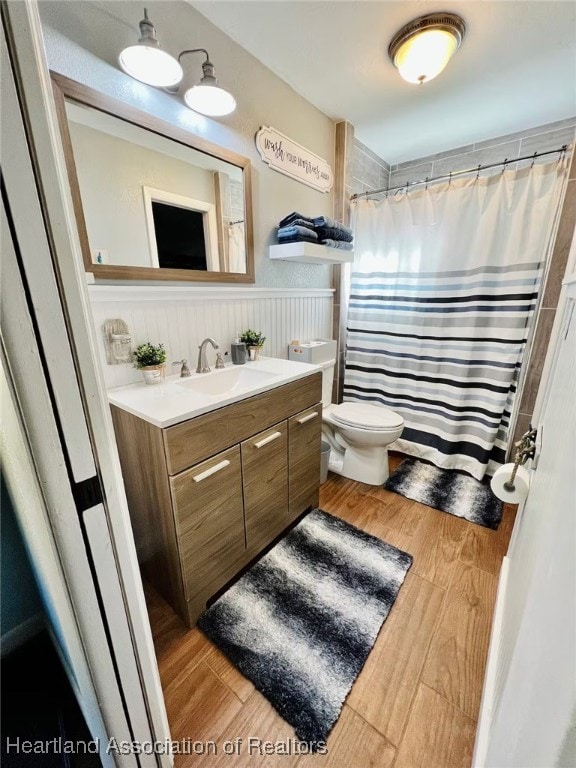 bathroom with toilet, a wainscoted wall, a shower with curtain, wood finished floors, and vanity