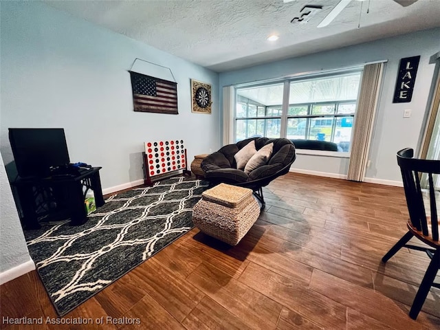 living area with a textured ceiling, wood finished floors, a ceiling fan, and baseboards