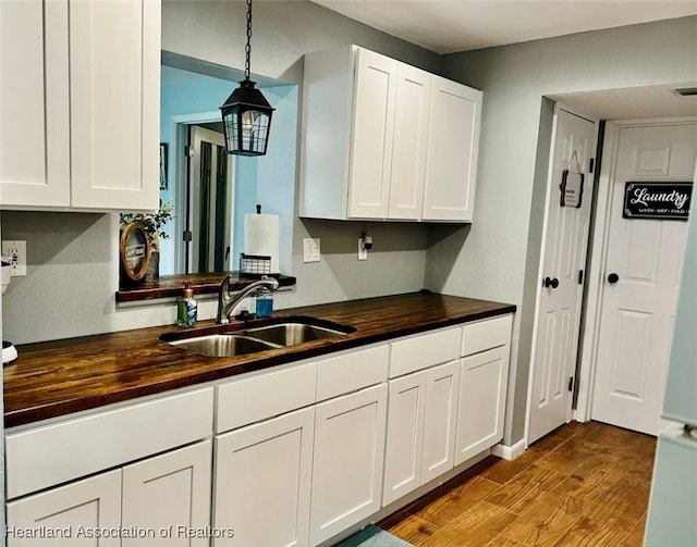 kitchen featuring butcher block countertops, decorative light fixtures, a sink, and white cabinetry