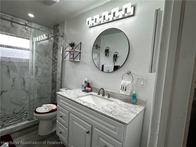 bathroom featuring vanity, hardwood / wood-style flooring, toilet, walk in shower, and a textured ceiling