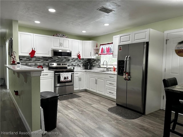 kitchen featuring tasteful backsplash, stainless steel appliances, sink, light hardwood / wood-style floors, and white cabinetry