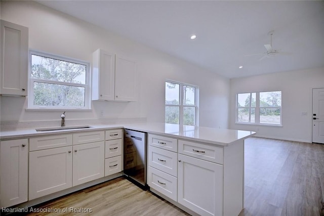 kitchen featuring dishwasher, light countertops, a peninsula, white cabinetry, and a sink