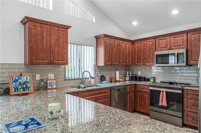 kitchen with lofted ceiling, light stone countertops, a sink, appliances with stainless steel finishes, and decorative backsplash